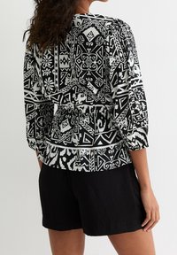 Blusa a maniche lunghe con motivo in bianco e nero, vita arricciata e orlo arrotondato. Tessuto testurizzato con design geometrici e floreali.