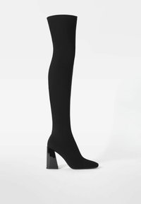 Botas negras por encima de la rodilla con un upper de tela lisa, puntera afilada y un tacón bloque grueso y brillante para mayor estabilidad.