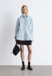 Light blue denim oversized shirt with buttons, black mini skirt, black handbag, and black loafers with brown socks. Smooth texture, relaxed fit.