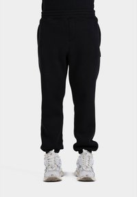 Pantaloni de trening negri cu talie elastică, buzunare laterale și manșete îngustate. Asortați cu pantofi sport albi cu un design texturat.