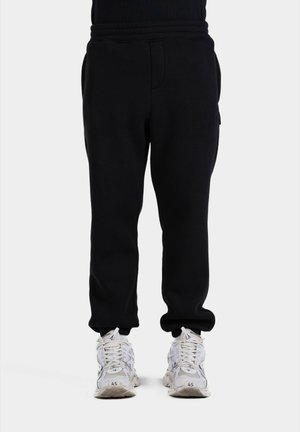 Svarta träningsbyxor med elastisk midja, sidofickor och smalnande mudd. Sammanställs med vita sportskor med en strukturerad design.
