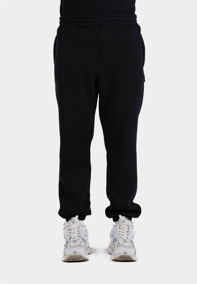 Pantaloni de trening negri cu talie elastică, buzunare laterale și manșete îngustate. Asortați cu pantofi sport albi cu un design texturat.