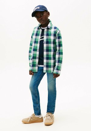 Groen en blauw geblokt overhemd over een marineblauw graphic t-shirt, gecombineerd met lichtblauwe skinny jeans en beige sneakers met witte veters.
