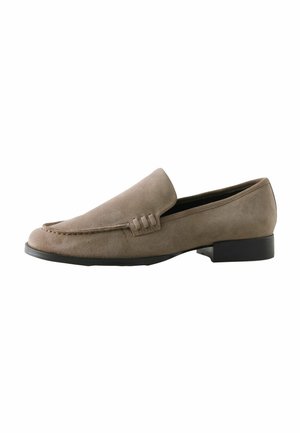 Mocassins en daim beige avec une texture lisse, présentant un détail de couture et une semelle noire basse. Design simple et classique à enfiler.
