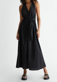 Schwarzer Halter-Jumpsuit mit tiefem V-Ausschnitt, elastischem Bund und gebundenem Gürtel. Verfügt über ein Design mit weitem Bein und glatter Textur.