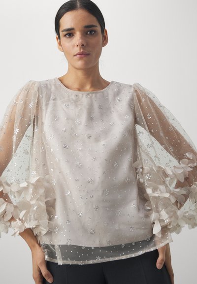 Sheer, light-colored blouse with puffed sleeves, featuring embroidered floral patterns and silver accents. Soft, delicate fabric flows elegantly.