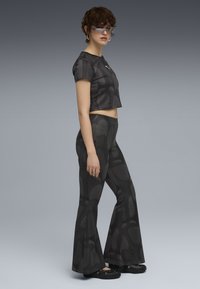 Black cropped shirt and flared pants with a textured dot pattern; paired with black clogs and sunglasses, showcasing a modern design.
