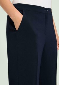 Marineblauwe broek met een gladde, gestructureerde stof, voorzien van een zijzak, strakke lijnen en een knoopsluiting in de taille.