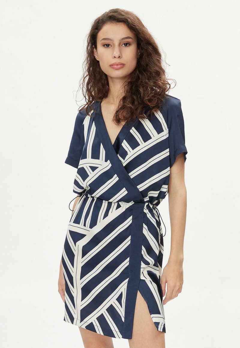Abito a portafoglio in navy con strisce geometriche bianche; maniche corte, vita elastica e dettaglio con spacco laterale. Tessuto dalla consistenza liscia.