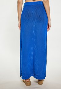 Gonna maxi all'uncinetto blu con un design a rete testurizzata, caratterizzata da un alta vita e spacco laterale per facilitare i movimenti. Indossata con espadrillas con zeppa.