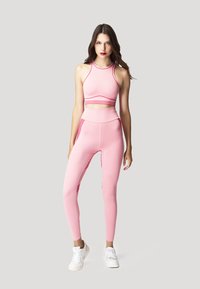 Completo sportivo rosa composto da un crop top aderente e leggings a vita alta con dettagli a strisce rosse. Realizzato in materiale elastico, offre un aspetto snello.