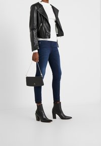 Chaqueta de biker de cuero negra, suéter blanco de canalé, jeans ajustados azul oscuro, botines negros de tacón y un pequeño bolso negro con cadena.
