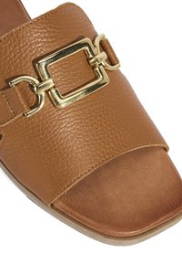 Braune Leder-Slidesandale mit strukturiertem Finish, offener Zehenpartie und einem dekorativen goldfarbenen Schließelement am Riemen.