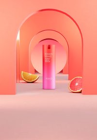 En rosa gradient flaske merket "Power Shake Pearly Magic Serum" er plassert i et livlig rosa bueopplegg, med appelsin- og grapefruktbiter ved siden av.