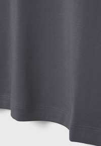 Tissu gris foncé avec coutures visibles le long de l'ourlet incurvé, montrant une texture fine tricotée et un ombrage subtil.