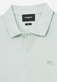 Ljusgrön pikétröja i texturerad tyg med en treknäppningsslå och en liten logotyp på vänster bröst. Slim fit-design.