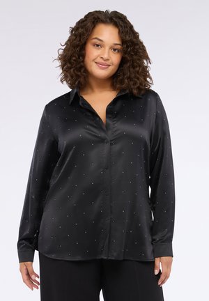 Camicia nera in satin a maniche lunghe con bottone frontale, caratterizzata da piccoli chiodini argento disposti in un motivo sparso su tutta la stoffa.