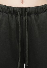 Tmavozelené teplákové nohavice s elastickým pásom a šnúrkou na stiahnutie. Vyrobené z mäkkej tkaniny, ktorá má hladkú textúru a minimalistic design.