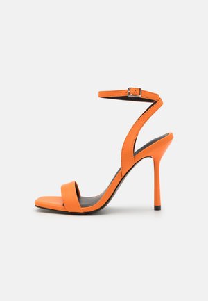 Orange højhælede sandaler med en enkelt rem over tæerne og en ankelrem. Har en slank stiletto-hæl og en glat lædertekstur.