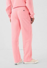 Roze sweatpants met een relaxed fit, een koord in de taille en een enkele achterzak. Zacht, geweven stof; gecombineerd met lichtgekleurde sneakers.