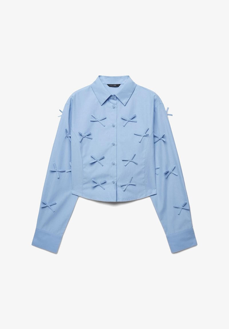 Light blue cropped shirt with long sleeves, button closure, and various bow accents on the front and sleeves. Smooth cotton fabric.