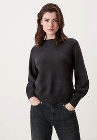 Donkergrijze gebreide trui met een brede halslijn en een ontspannen pasvorm, voorzien van geribbelde manchetten en zoom. Gecombineerd met zwarte denim broek.