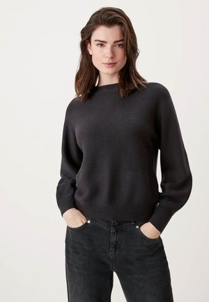 Donkergrijze gebreide trui met een brede halslijn en een ontspannen pasvorm, voorzien van geribbelde manchetten en zoom. Gecombineerd met zwarte denim broek.