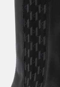 Botte noire avec une élégante finition en cuir et un panneau textile noir à motifs, présentant un design texturé et des coutures détaillées.
