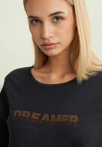 T-shirt in cotone nero con la scritta "DREAMER" in strass sfumati, scollatura rotonda e maniche corte. Tessuto morbido e vestibilità rilassata.