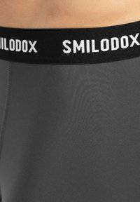Grå herreundertøj med en sort elastikaf bæltet, som har "SMILODOX"-logoet i hvidt. Stoffet ser glat ud med en let glans.