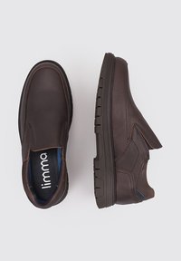 Zapatos marrones de cuero tipo slip-on con acabado texturizado. Cuentan con suela de goma, forro interior azul y costuras decorativas.