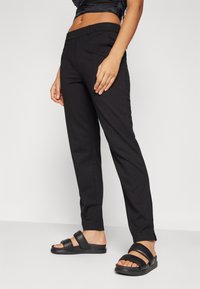 Černé dobře padnoucí kalhoty se hladkým povrchem a zúženými nohavicemi, doplněné černými skládacími sandály s širokými popruhy.