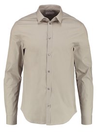 Beige långärmad skjorta med klassisk krage och sju knappar framtill, visad på en vit bakgrund.