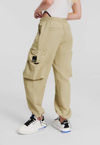 Beiga cargobyxor med elastisk midja, två stora sidofickor och en slät yta, tillsammans med vita sneakers med svarta detaljer.