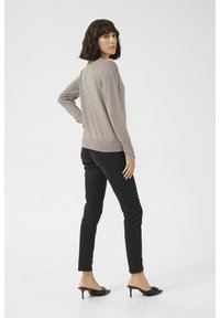 Maglione beige lavorato a maglia con maniche lunghe, design aderente e orlo a costine; abbinato a jeans neri slim e mule nere con tacco.