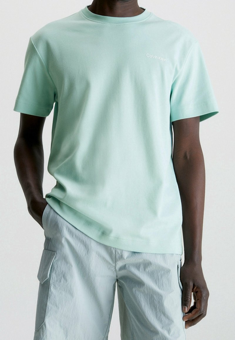 Mátově zelené bavlněné tričko s kulatým výstřihem a krátkým rukávem, s malým bílým logem na hrudi a volným střihem.