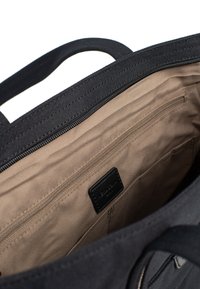 Borsa tote nera in tessuto con un interno beige, dotata di una tasca con zip e di una piccola etichetta in pelle. Le maniglie sono robuste e dritti.