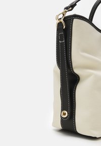 Canvashandväska med svarta läderdetaljer, i krämfärg. Den har kontrasterande sömmar, en detaljer i guld-ton och en mjuk, strukturerad form.