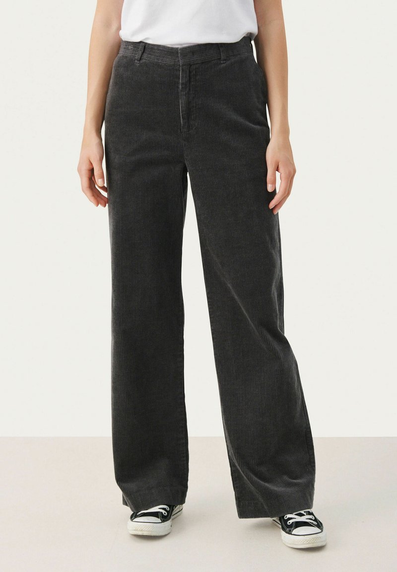 Pantalons en velours côtelé noir à jambe large avec des côtes verticales, poches avant et ceinture. Assortis à des baskets en toile noires.