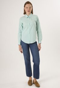 Chemise à carreaux verte et blanche avec des manches longues, associée à un jean droit bleu et des chaussures slip-on marron.