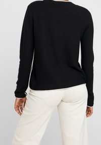 Svart långärmad tröja med rundad halsringning och kontrasterande vit kant längs nederkanten och manschetterna; visad bakifrån.