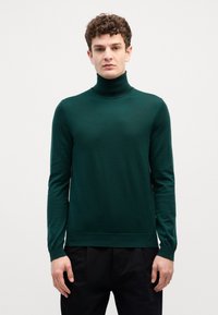 Dunkelgrüner Rollkragenpullover aus einem weichen, strukturierten Strick. Mit langen Ärmeln und figurnaher Silhouette. Einfaches, klassisches Design mit gerippten Bündchen.