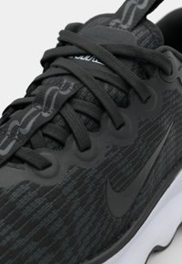 Black athletic shoe featuring textured synthetic upper, flat laces, and a prominent logo, with a contrasting white sole and flexible accents.