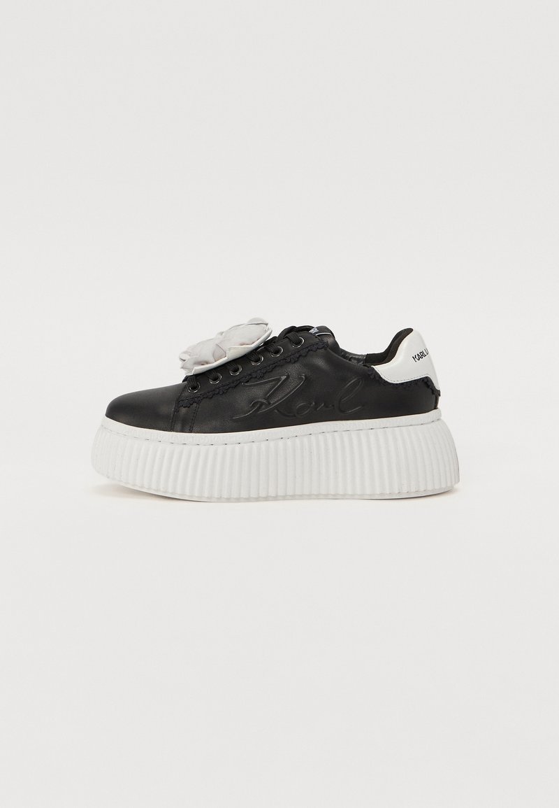 Sorte lærersneaker med hvit ribbet såle, med en blomsterdetalj på tungen og "Karl" preget på siden.