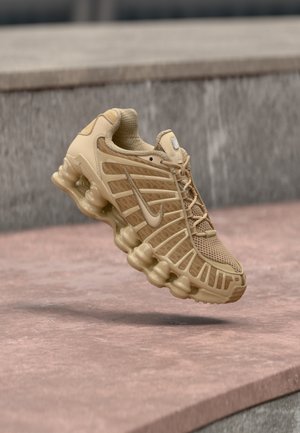 Beige sportieve schoen met een mesh bovenwerk en gestructureerde ondersteuning, voorzien van een geveerd zool met zichtbare luchtkussens en een textuurdetail.