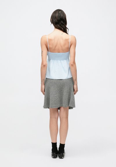 Svetlomodrý top bez rukávov s načechraným živôtikom, doplnený sivou rozšírenou sukňou. Oblečenie má jednoduchý dizajn a mäkké textúry.