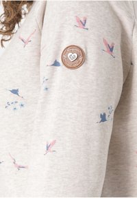 Felpa grigia chiara con motivi di uccelli rosa e blu. Presenta un distintivo tondo in pelle marrone con testo in rilievo sulla manica sinistra.
