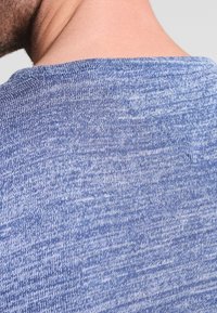 Tissu tricoté bleu clair présentant un motif texturé légèrement chiné, avec un large col rond et une finition lisse au bord.