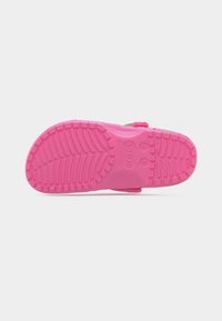 Σόλα ενός ροζ παπουτσιού Crocs που δείχνει το μοτίβο του πέλματος, τις σημάνσεις μεγέθους και ένα λουράκι στη φτέρνα σε λευκό φόντο.