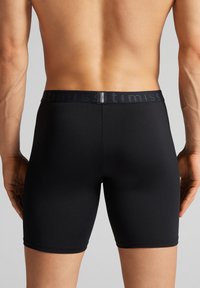 Černé boxerky vyrobené z hladké, pružné tkaniny. Mají široký elastický pás s jemným brandingem podél horního okraje.